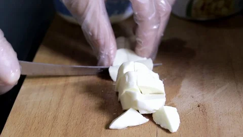 A hand in gloves cuts cheese into cubes Stock Footage 93220617