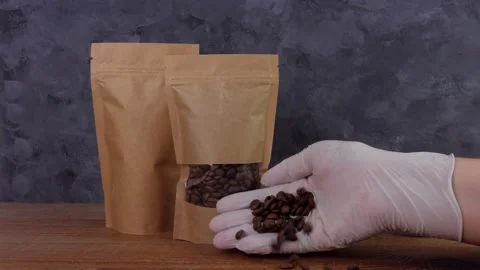 Hand in gloves spills coffee beans shows thumb up Kraft paper pouch bag mockup Stock Footage 148726536