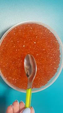 The hand is going to take the red caviar with a spoon from a large jar Stock Photos