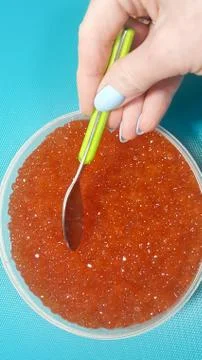 The hand is going to take the red caviar with a spoon from a large jar Stock Photos