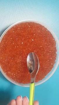 The hand is going to take the red caviar with a spoon from a large jar Stock Photos
