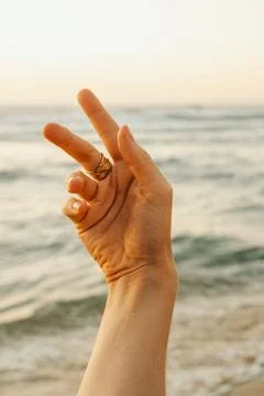 A hand with a gold ring points towards the ocean. The sun is setting in the b Stock Photos