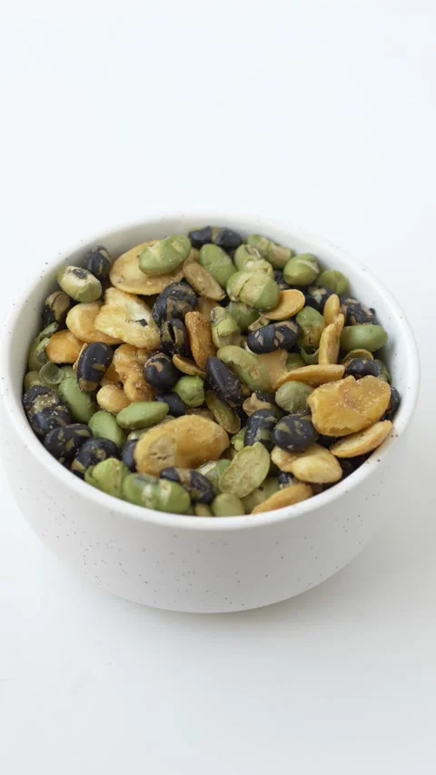 Hand grabbing mixed bean snack from white bowl as healthy plant-based protein Video stock 331010414