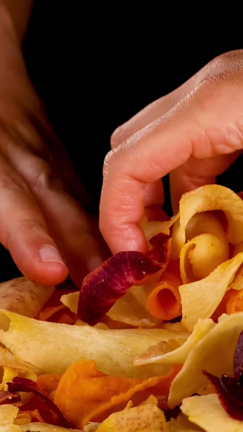 Hand Grabbing Mixed Root Vegetable Chips Against Black Background Stock Footage 323347701