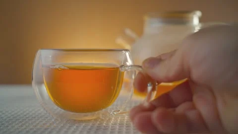The hand grabs a glass mug which already has some freshly brewed tea in it. Stock Footage 295457749