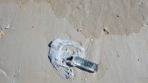 A hand grabs a plastic bag and plastic bottle dumped on the beach Stock Footage 111181704