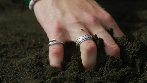 A hand grasps dark soil, adorned with beautiful jewelry accents, creating a Stock Footage 305432247
