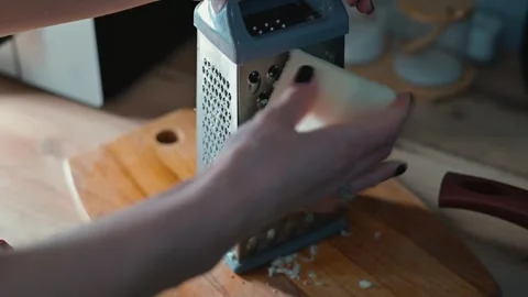 A hand grates cheese on a box grater while standing at a wooden cutting board. Stock-Footage 339094524
