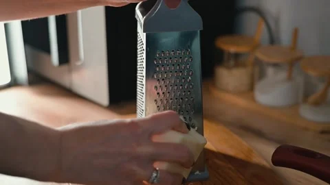 A hand grates cheese using a box grater in a kitchen setting. The focus is on Stock Footage 339094519