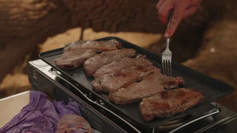 Hand grilling steaks with fork on portable gas stove outdoors Stock Footage 337912464