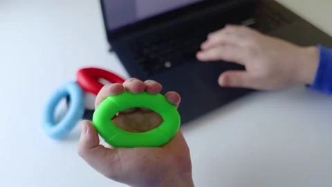 Hand gripper. Man squeezes rubber expander while working on his laptop. Concept  Stock Footage 265652597