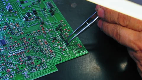 Hand gripping tweezers assembling electrical parts on detailed surface of Stock Footage 214104333
