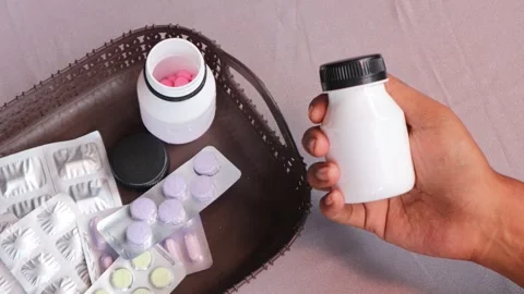Hand gripping a white pill bottle surrounded by various medications. Stock Footage 340796732