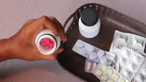 Hand gripping a white pill bottle surrounded by various medications. Stock Footage 340796734
