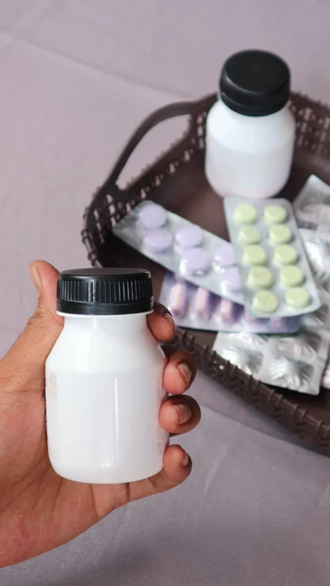Hand gripping a white pill bottle surrounded by various medications. Stock Footage 340796775