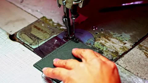 Hand guides fabric or leather piece under sewing machine needle stitching edge Stock Footage 332755411