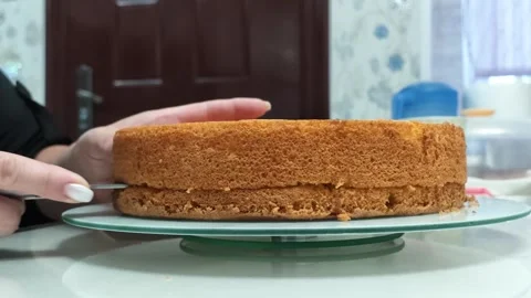 Hand guiding knife to slice thick sponge cake on glass plate in bright home Video stock 343516394
