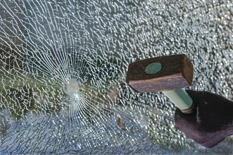 Hand with a hammer and a broken window made of safety glass, concept for Stock Photos
