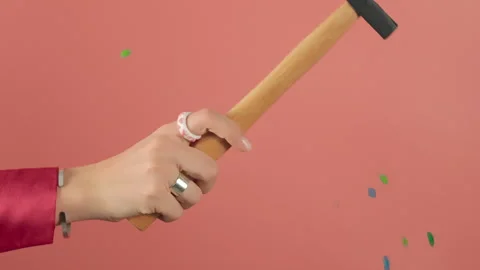 A hand with a hammer on a pink background hits small multi-colored round candies Stock Footage 256183604