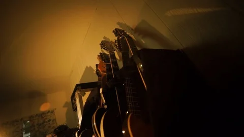 A hand held camera tilts down a row of guitars in a garage band practice Stock Footage 102828302