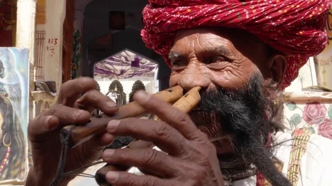 Hand-held CU Rajasthani elderly male plays the flute with his nose Stock Footage 69767543