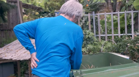 Hand held of an elderly man rubbing his back while working in the yard Stock Footage 61627527