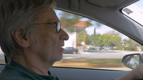 Hand held of an elderly senior man driving a car during the day and talking Stock Footage 61493666