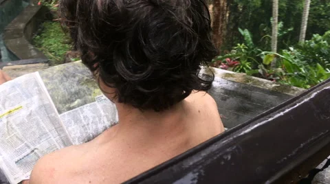 Hand held shot of man refusing to leave the pool with his magazine in the rain Stock Footage 61120584