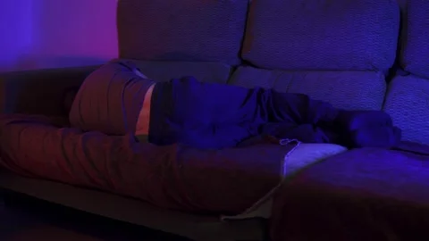 Hand-held shot of a tired man sleeping on the couch with the tv on 스톡 동영상 219026893