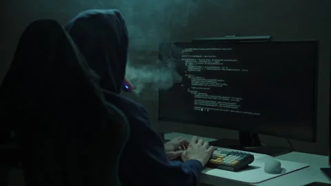 Hand held shot of unrecognizable hacker in dark hood working on computer at Stock Footage 323449858