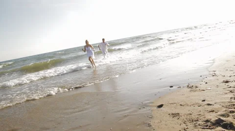 Hand held shot of young couple running and chasing on beach Stock Footage 43619181