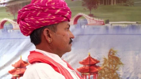 Hand-held side profile with a red turban with a colourful tent backdrop Stock-Footage 69786409