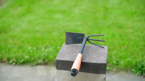 Hand hoe close-up against the background of a green well-groomed lawn. Double Stock Footage 230206400