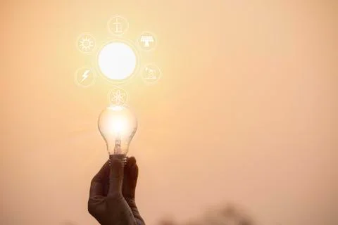 Hand hold a light bulb on sunset background for saving energy and creative co Stock Photos
