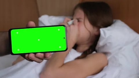 Hand hold phone with green screen mock up, Sick kid girl on bed on background Stock Footage 301893746