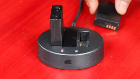 Hand holding and inserting a rechargeable battery into a black charging dock Stock Footage 348155624