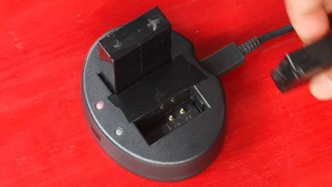 Hand holding and inserting a rechargeable battery into a black charging dock Stock-Footage 348155632