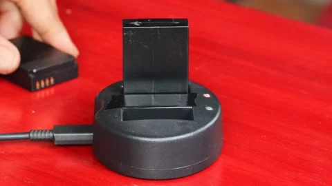 Hand holding and inserting a rechargeable battery into a black charging dock Stock-Footage 348155636