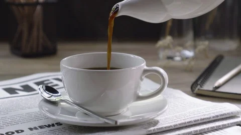 Hand holding and pouring hot coffee Into white cup on newspaper Stock Footage 104841953