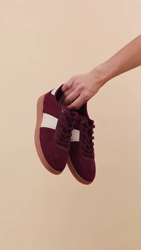 Hand holding and rotating maroon suede sneakers in studio Video stock 331774016