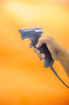 A hand holding a barcode scanner against an orange background, showcasing i.. 库存照片