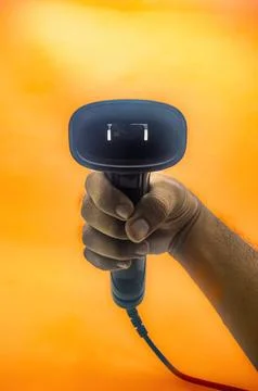 A hand holding a barcode scanner against an orange background, highlighting.. 库存照片
