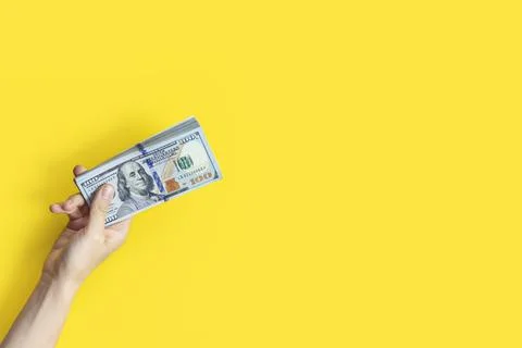 Hand holding a big stack of banknotes isolated on yellow background. Wealth or Stock Photos
