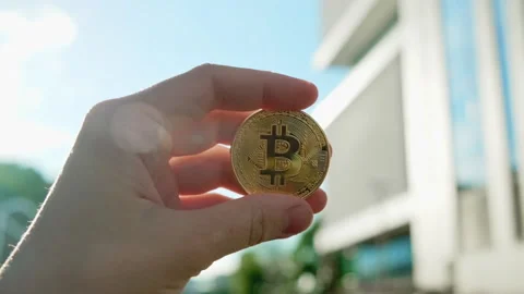 Hand holding a Bitcoin in front of a modern building Stock Footage 328268963