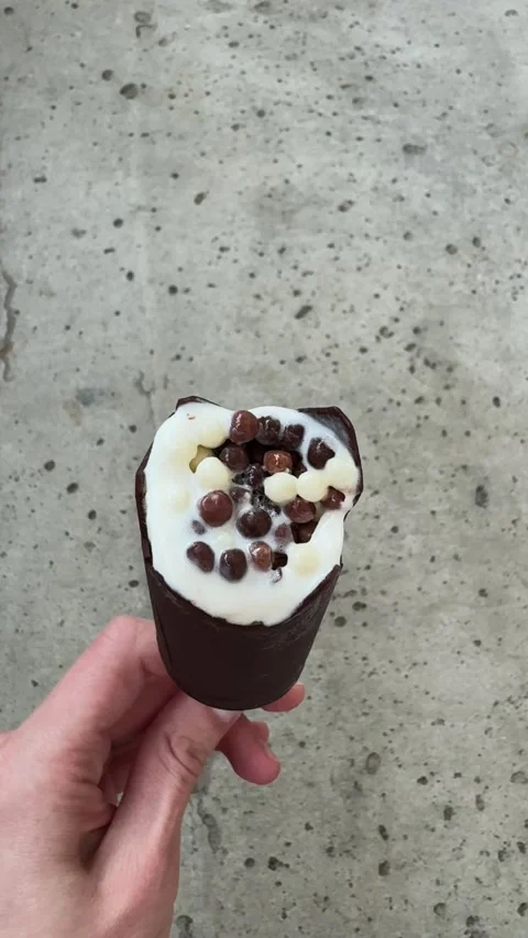 Hand holding bitten chocolate ice cream with vanilla filling  Vídeo Stock 336796103