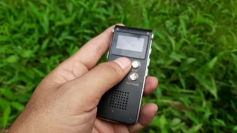 Hand Holding Black Digital Voice Recorder in Grassy Background Video stock 309913656