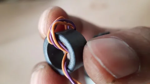Hand holding a black ferrite toroid core with thin purple and orange copper.. Stock Footage 324824637
