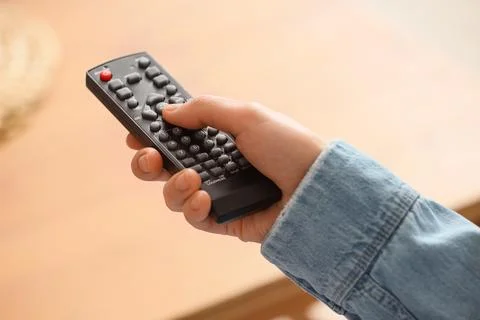 Hand holding black remote control with red power button, changing channels an Stock Photos