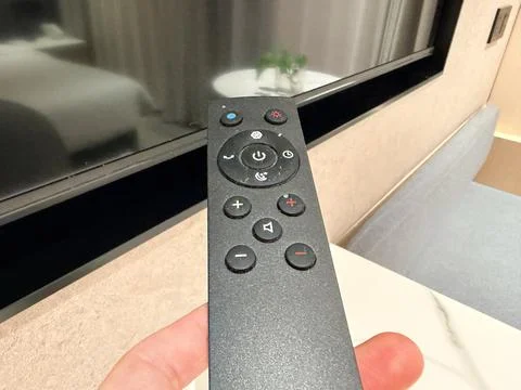 Hand Holding a Black Remote Control in Front of a TV Stock-Fotos