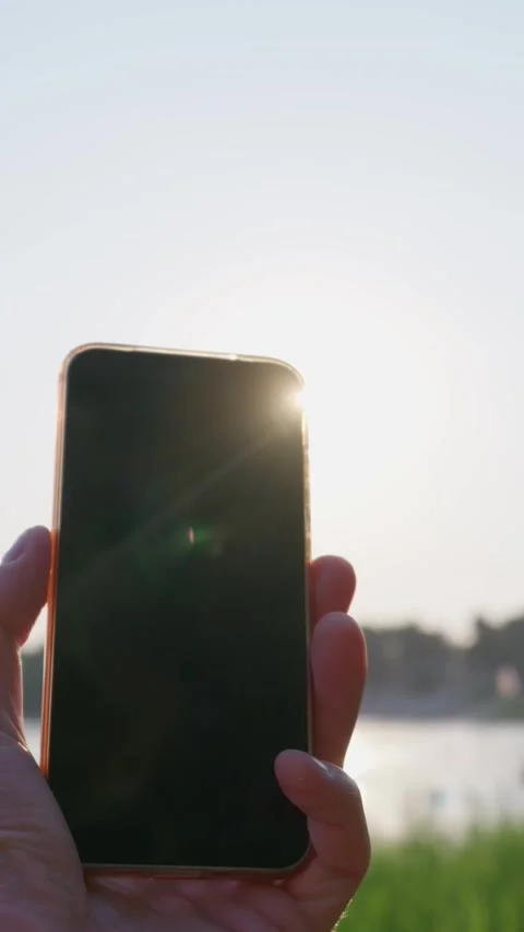 Hand Holding Blank Smartphone Screen in Bright Sunlight Outdoors at Lake Stock Footage 343564647